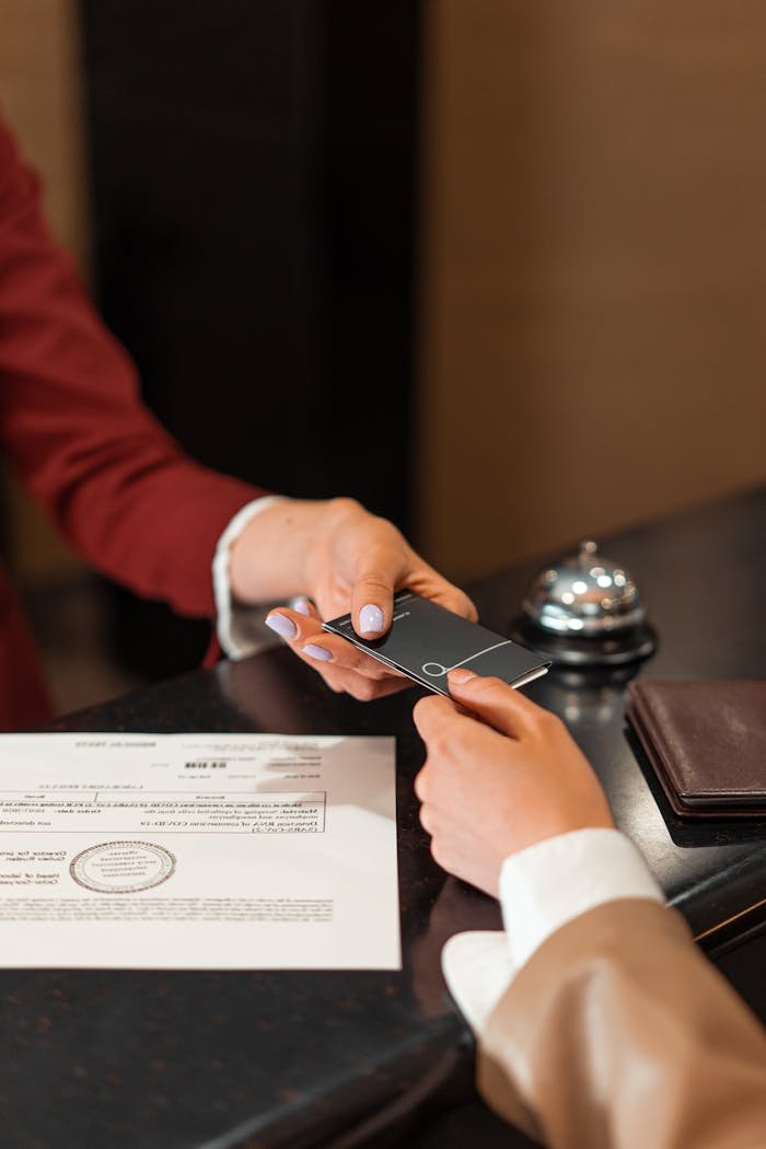 services-04 A hotel receptionist hands a key card to a guest over the counter, with documents visible.